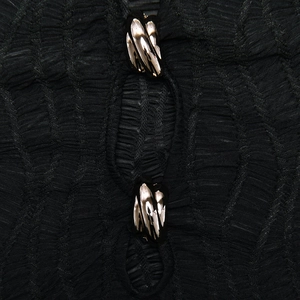 Détail d'une robe en tissu noir texturé avec deux attaches métalliques dorées torsadées