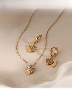 Detail shot of heart necklace and earrings set with zircons on a textured background