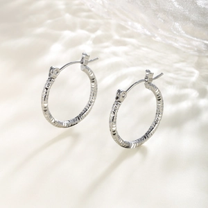 Macro shot of silver hoop earrings with diamond-cut chain texture on silk surface