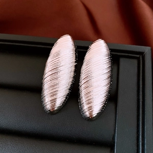 Gros plan de boucles d'oreilles ovales argentées à texture rainurée sur cuir noir