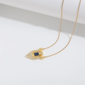 Macro detail of gold geometric shield pendant with blue rectangular stone and small white zircons