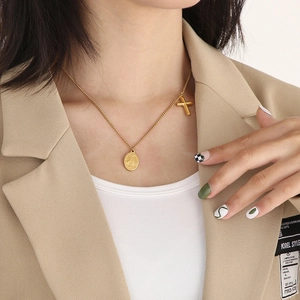 Close-up of golden oval medallion and cross pendant necklace worn by a model