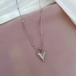 Macro shot of polished silver heart pendant with bead chain on elegant satin background