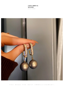 Détail de boucles d'oreilles dorées en zircone avec de grandes perles grises élégantes