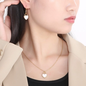 Close-up of model wearing gold heart pendant necklace and matching stud earrings set