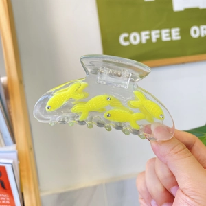 Detailed close-up of transparent acetate fish hair claw with yellow accents and rhinestones