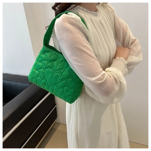 Détail du sac à main matelassé vert avec textures à motifs de cœur sur fond de robe blanche