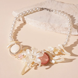 Close-up of pearl necklace featuring resin flower and shell pendant on stone