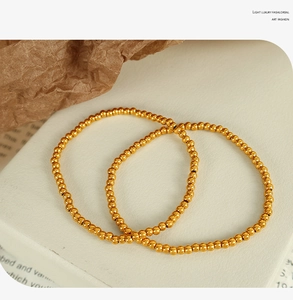 Macro shot of dual golden metallic bead bracelets on elegant vintage paper background