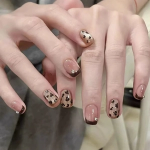 Faux ongles léopard style français avec bouts marrons et petits strass sur les mains
