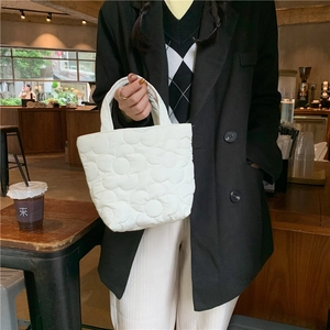 Detail of white quilted tote bag with floral patterns on a wooden cafe table