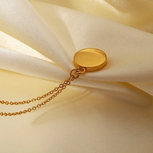 Macro shot of 18K gold plated necklace with round pendant on champagne silk fabric