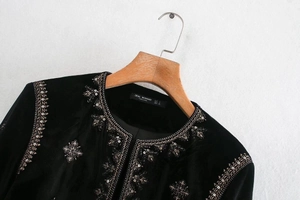 Détail d'une veste en velours noir avec broderies dorées complexes et ornements pailletés