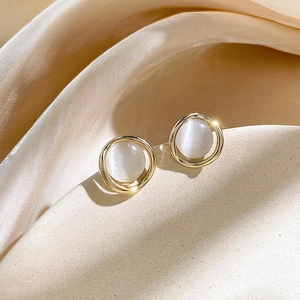 Detail of gold cat-eye earrings on beige silk fabric showing elegant geometric design