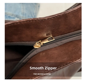 Close-up of a smooth gold metal zipper on a brown textured leather tote bag detail