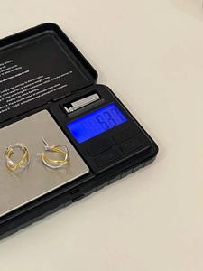 Detailed view showing a pair of silver and gold earrings on a scale weighing 8.30g
