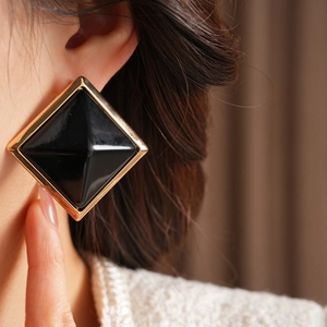 Close-up of square geometric stud earring featuring black resin and gold metal borders
