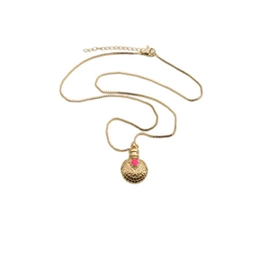 Detail view of a gold hollow round pendant with a pink gemstone on a box chain