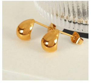 Macro shot of polished gold water drop earrings on a minimalist cream background