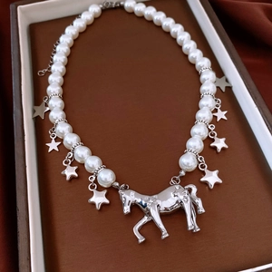 Détail d'un collier de perles blanches avec pendentif cheval argenté et petites étoiles