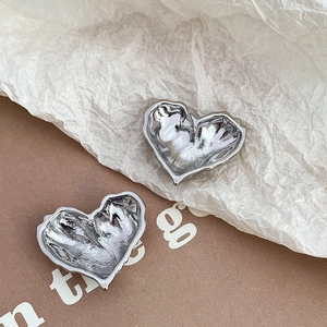 Close-up of heart-shaped silver earrings with unique lava texture and pleated metal detail