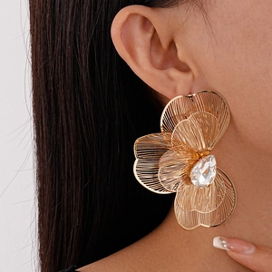Detailed close-up of oversized gold hollow flower earrings with large teardrop crystal
