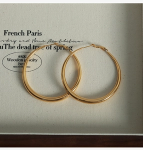 Vue détaillée de grandes boucles d'oreilles créoles dorées dans une boîte à bijoux en bois
