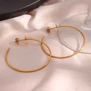 Close-up of golden stainless steel hoop earrings with cross charm on pink silk fabric