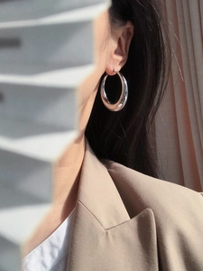 Close-up of minimalist chunky silver oval hoop earrings worn by a model in a studio setting