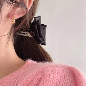 Close-up of a black mesh bow hair claw clip and gold twist hoop earrings worn by a model