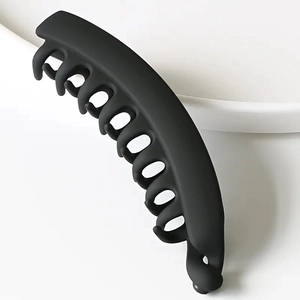 Minimalist matte black vertical banana clip for women on a white ceramic bowl edge