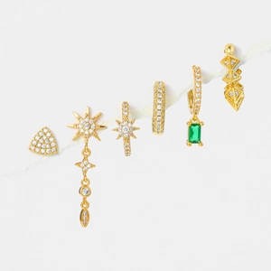 Gold geometric earrings set with cubic zirconia and green stones on marble background