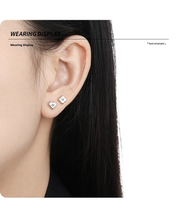 Wearing display of asymmetric silver clover and heart stud earrings with small zircon stones