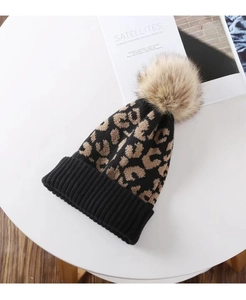 Detailed close-up of leopard print knit beanie with fluffy faux fur pompom and ribbed cuff