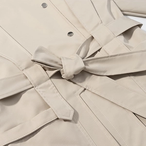 Nahaufnahme des beigen Trenchcoats mit Bindegürtel und Details der Metalldruckknöpfe