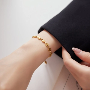 Detailed close-up of a golden coffee bean chain bracelet worn on a woman's wrist