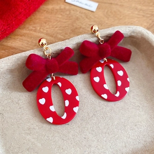 Détail de boucles d'oreilles nœud rouge floqué avec cœurs blancs sur métal doré