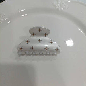 Detail of pearl white hair claw clip with pink floral rhinestones on white ceramic tray