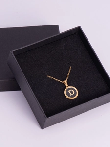 Close-up of gold letter D pendant on black circular base in a square gift box