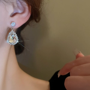 Close-up of silver waterdrop crystal earrings with rhinestone border worn by a model