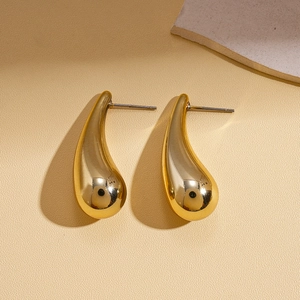 Detailed view of polished golden water drop stud earrings on a textured minimalist background