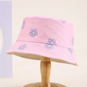 Pink kids bucket hat with purple smiley flowers on a wooden stand in soft light