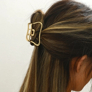 Elegant gold metal hair claw clip with geometric cutout design worn by a model