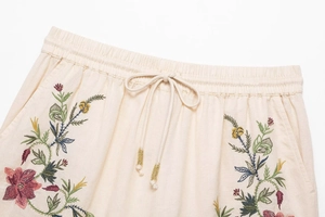 Detail of beige cotton linen shorts with floral embroidery and drawstring with gold beads