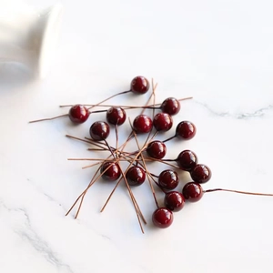 Deep red artificial 8mm berries with brown wire stems on white marble background