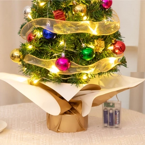 Close-up of a 55cm mini Christmas tree with warm lights, colorful baubles, and gold base