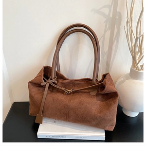 Detail shot of a large brown suede tote bag placed on a book with minimalist decor