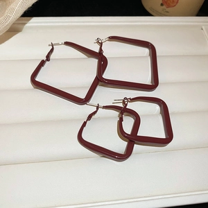 Macro shot of geometric burgundy red square enamel hoop earrings on a leather display