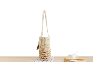 Detail of bohemian hand-woven cylinder water bottle bag on a wooden table setup