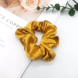 Close-up of a large golden satin scrunchie placed on an open magazine for hair styling